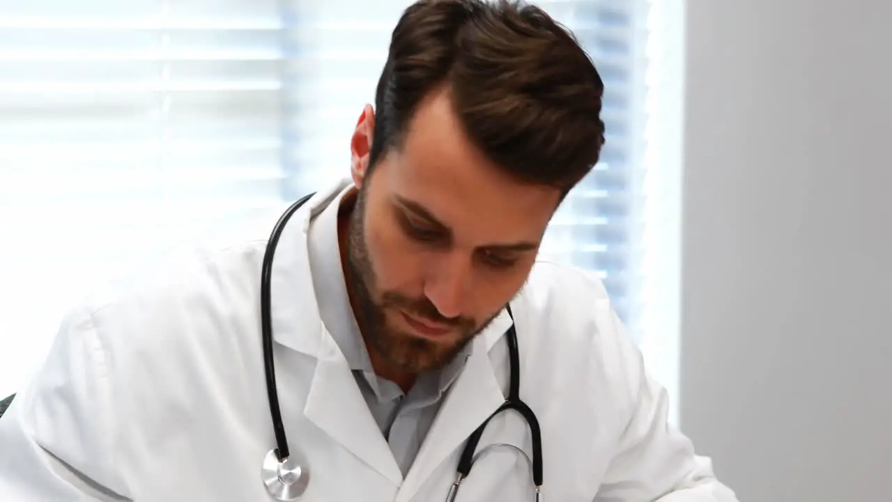 Male doctor writing on clipboard at desk