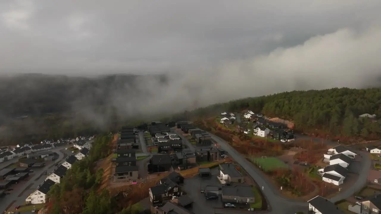 Drone footage of housing estate in Norway with some fog floating in th air and sun lighting up the clouds