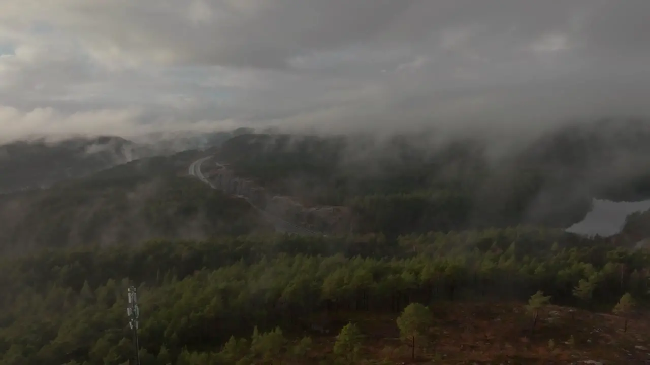 Drone footage of highway radiotower and housing estate in Norway with some fog floating in the air and sun lighting up the clouds