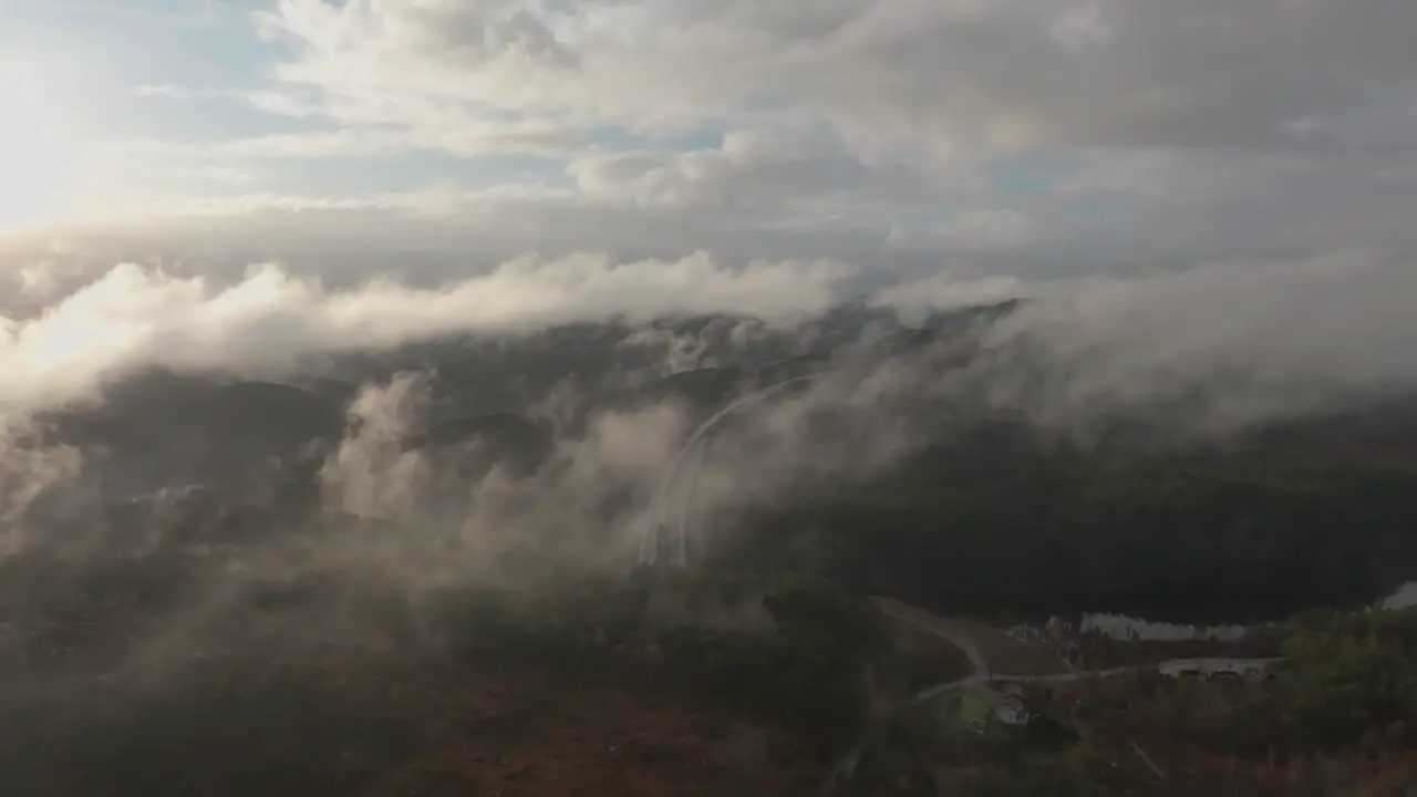 Drone footage of highway and housing estate in Norway with some fog floating in the air and sun lighting up the clouds