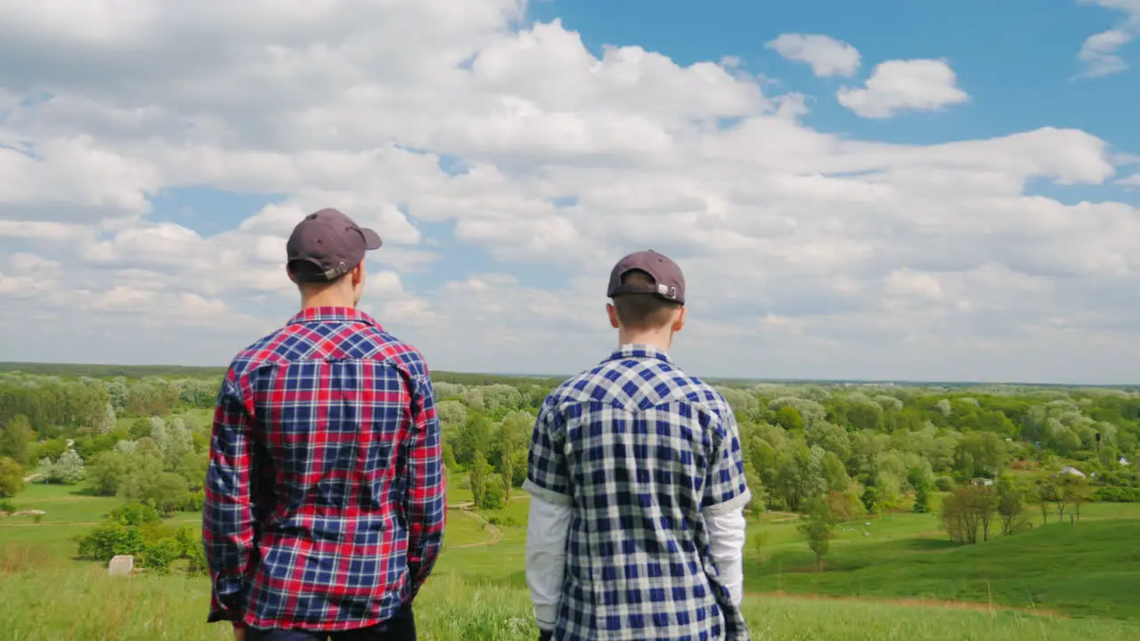 Two Young Men Stand On Top Of A Green Mountain 1