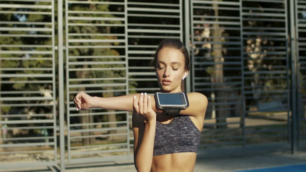 Sporty Woman With Airpods Warming Up And Stretching Arms At Sport Court On Summer Morning