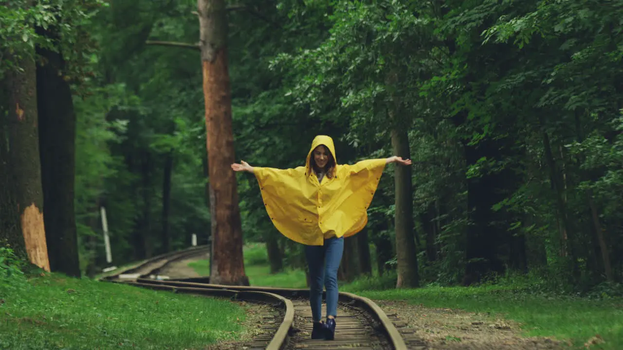 Charming Girl In A Yellow Raincoat Running And Walking Happily On The Old Railway In The Forest