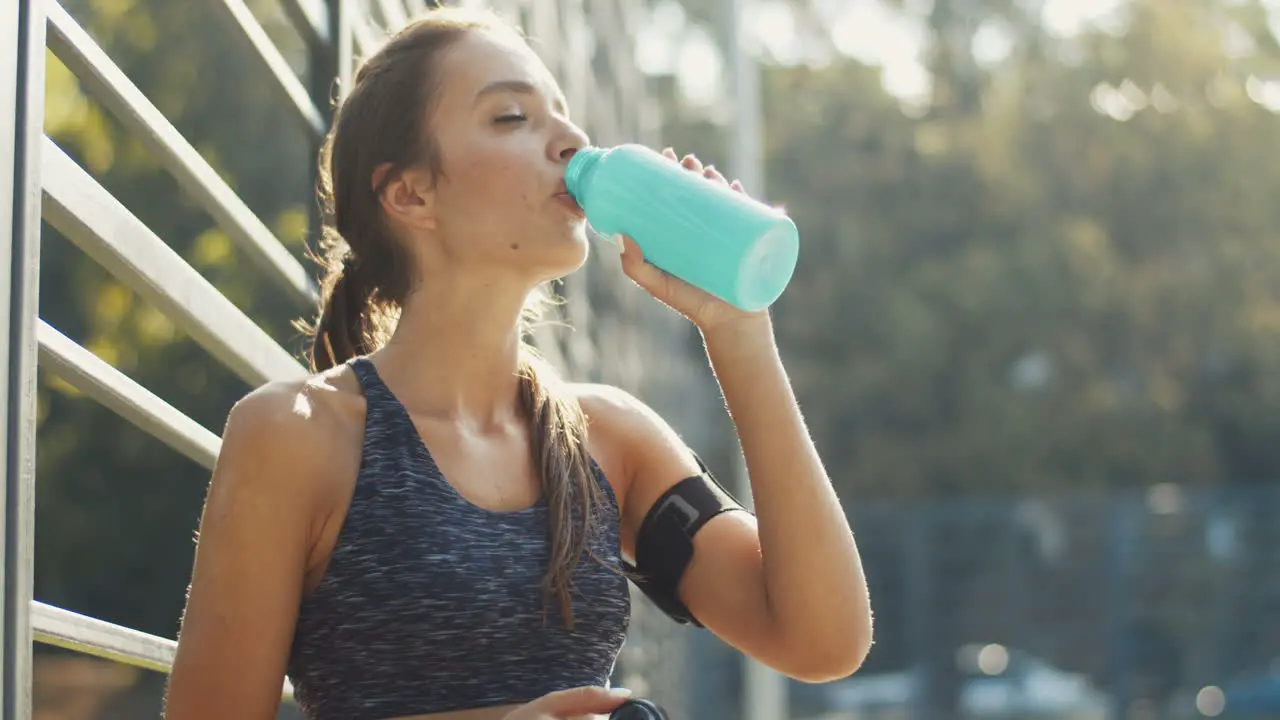 Tired Sporty Woman Standing At An Outdoor Court Resting And Drinking Cold Water After Workout