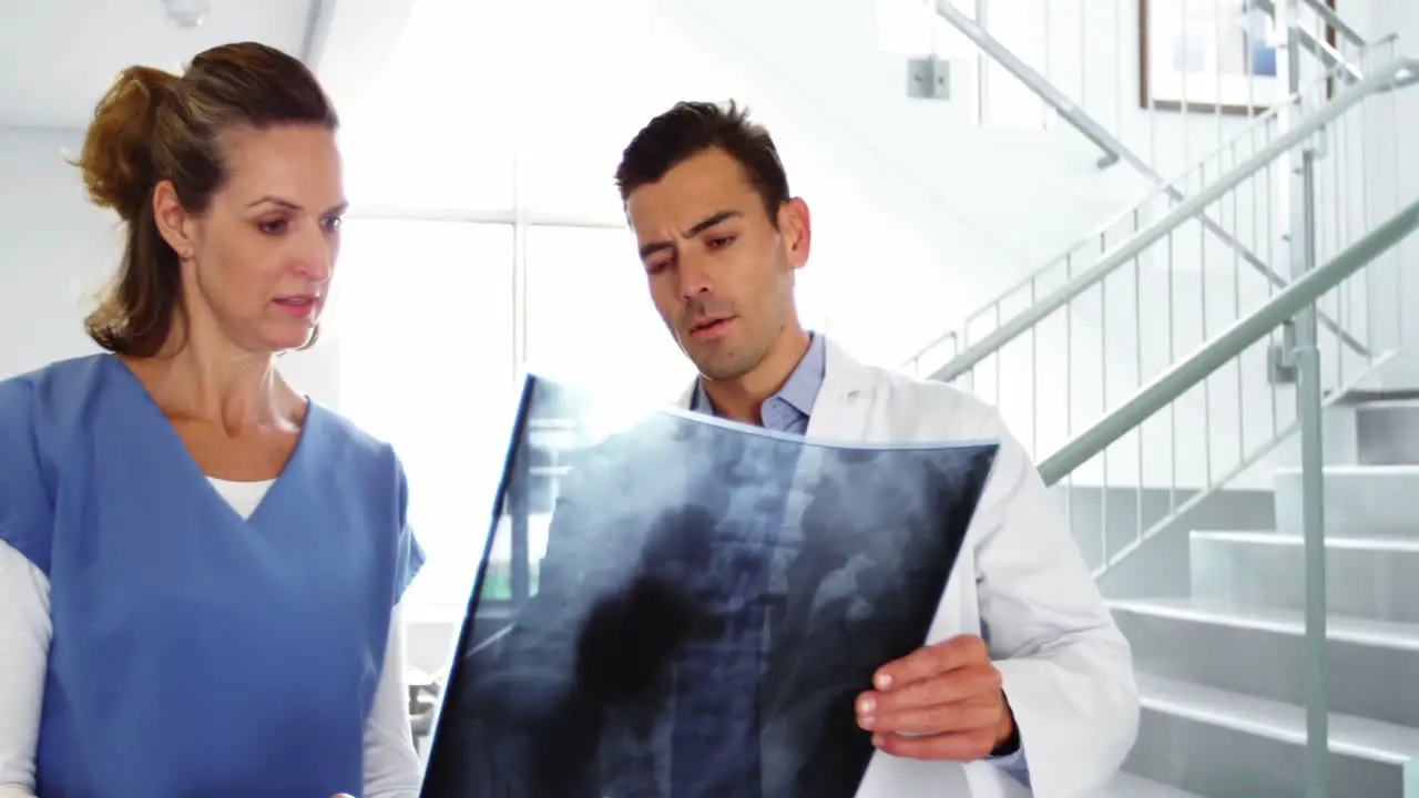 Doctor and nurse discussing over x-ray report in corridor