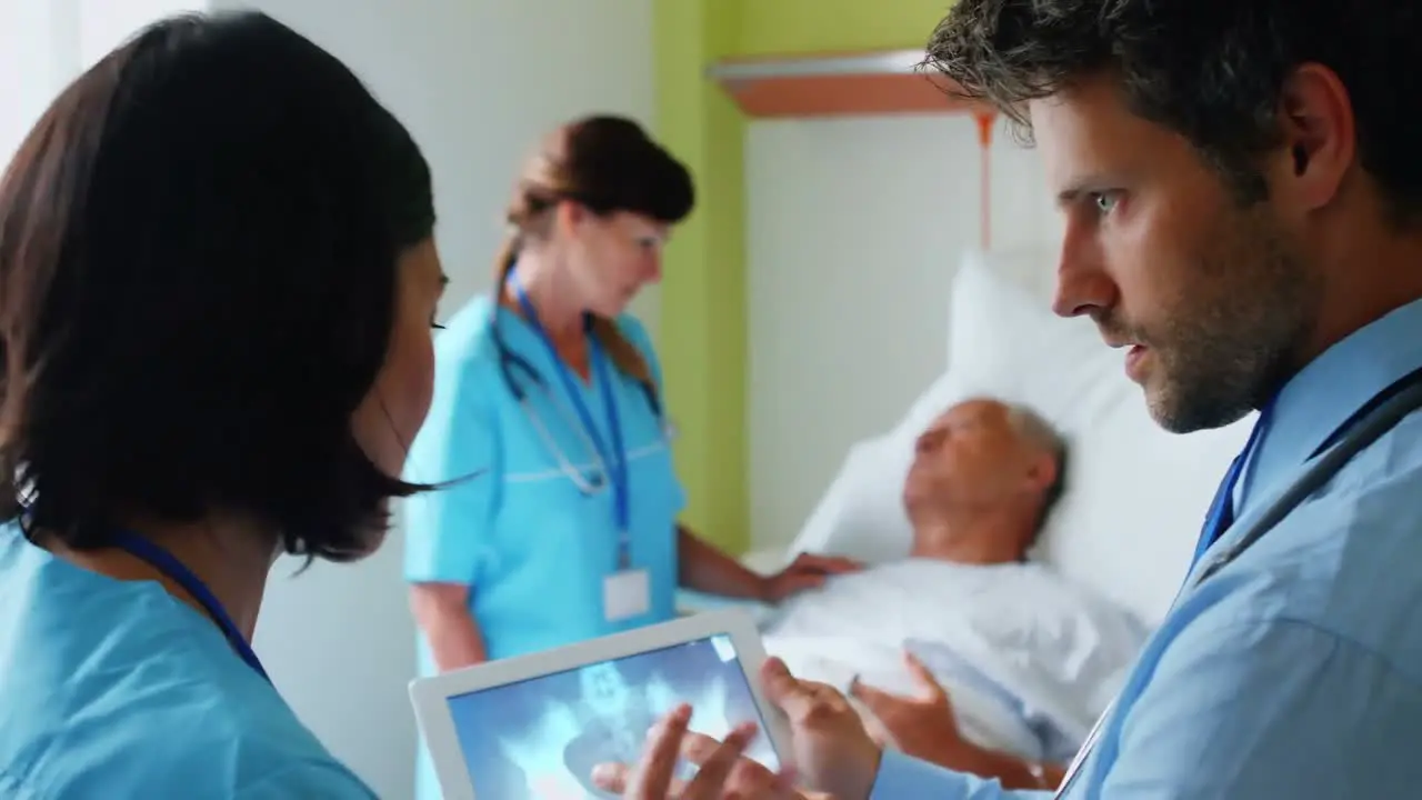 Doctors discussing x-ray on digital tablet while nurse interacting with patient in background