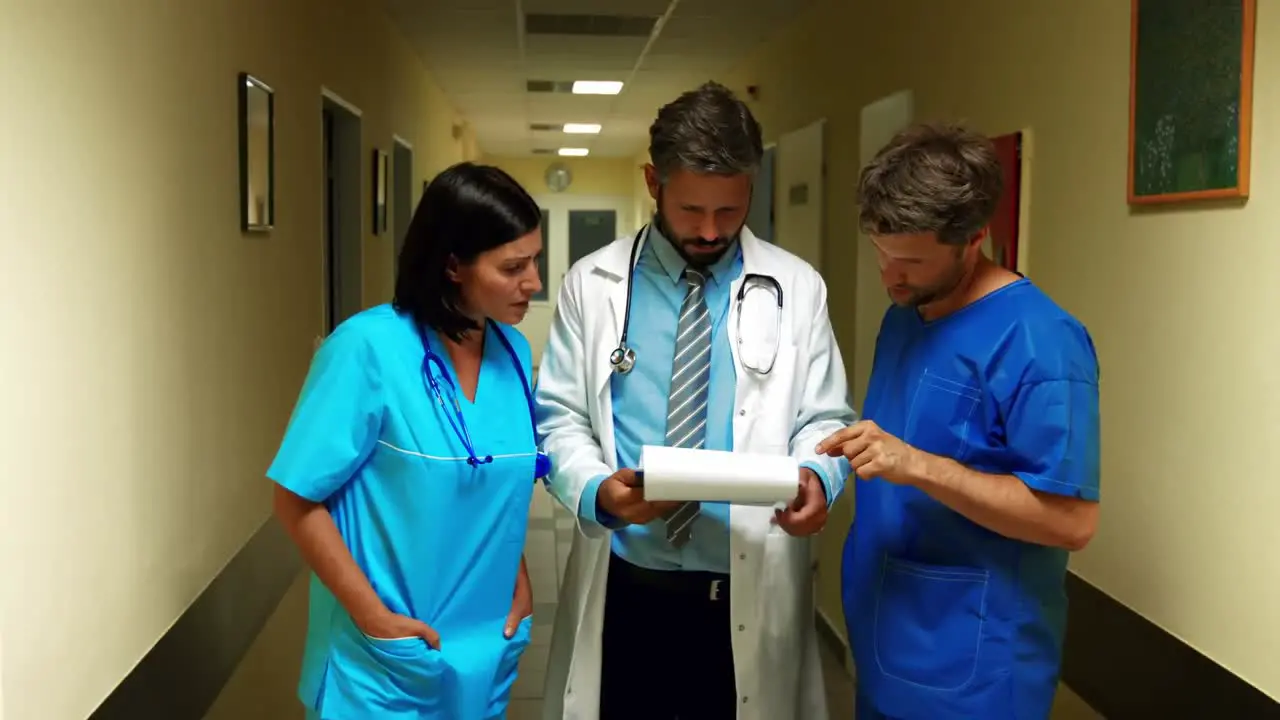 Doctor interacting over a report with ward boy and nurse in corridor