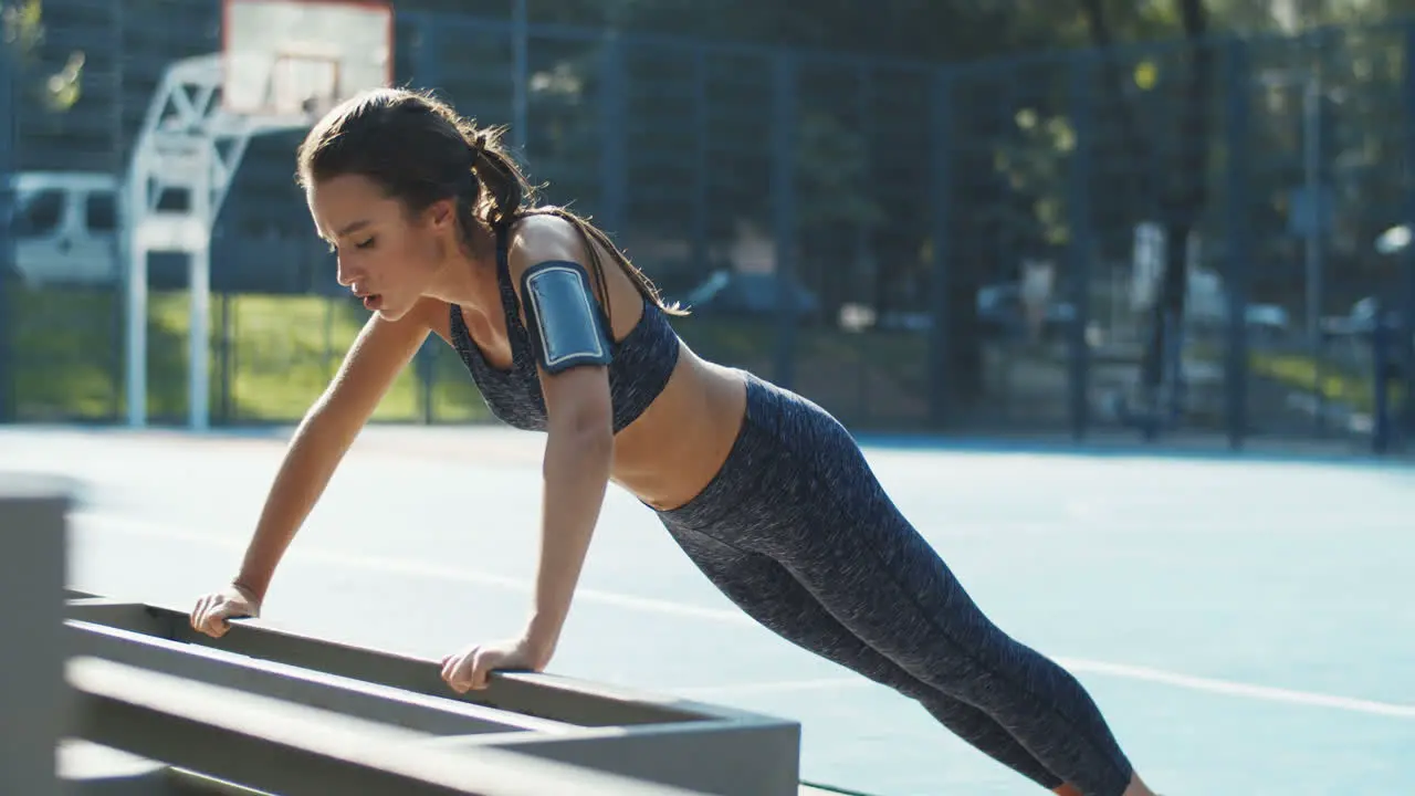 Sporty Girl Doing Push Ups From Bench At Outdoor Basketball Court In Summer Morning