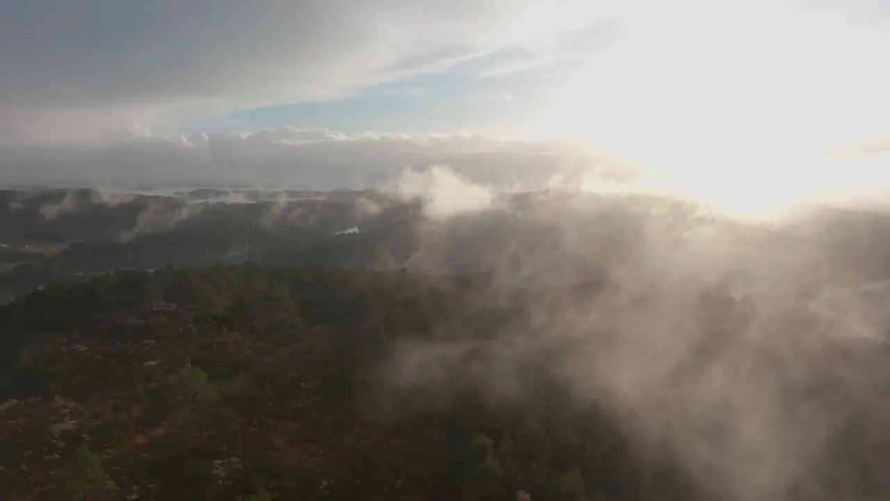 Drone footage of a radio tower and housing estate in Norway with some fog floating in th air and sun lighting up the clouds