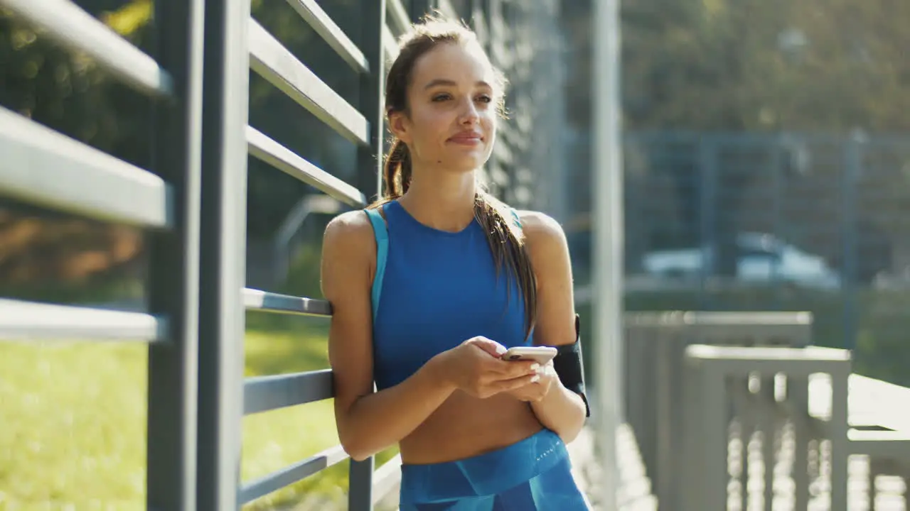 Pretty Sportswoman Texting Message On Smartphone And Smiling At Outdoor Court On A Summer Day