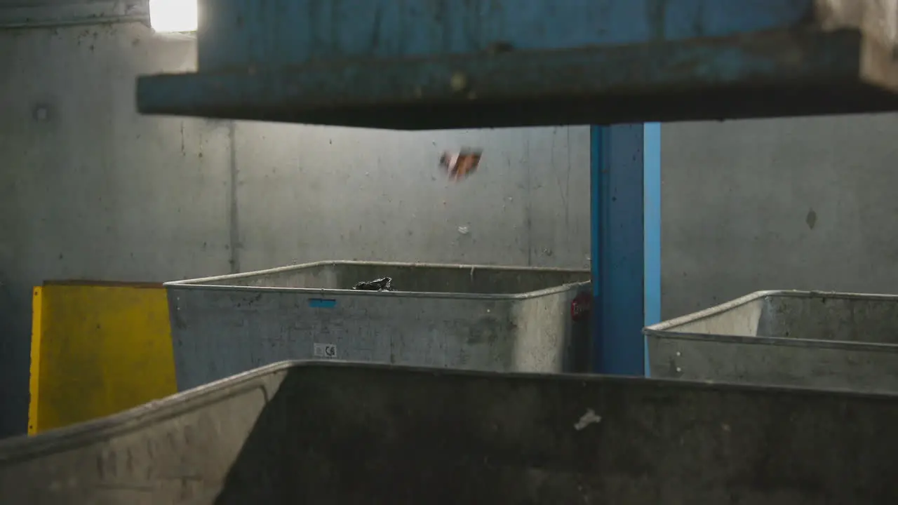 Plastic bags and trays drop into a metal container at a recycling factory