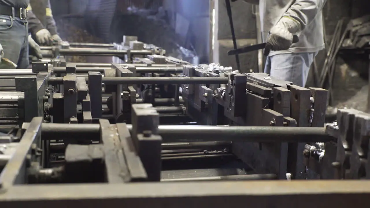 Side view of people removing metal objects from moulds in a factory