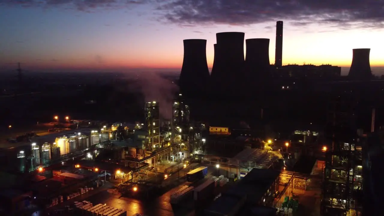 Illuminated aerial night view above industrial pipeline chemical factory site push in tilt down