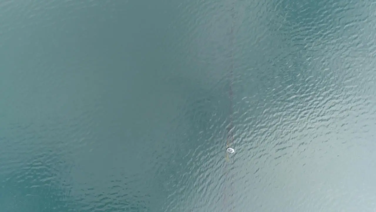 Topdown aerial along calm textured loch water following the line of a fishnet with buoys attached