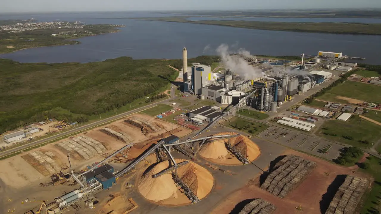 Aerial view of Paper Mill Factory with smoky chimneys front to River Sawdust piles and pipes transporting wood trunks