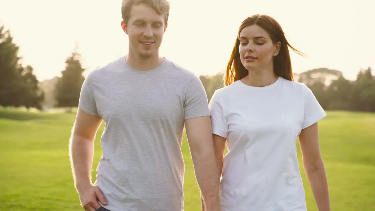 Happy Couple Holdings Hands And Talking While Walking Together Towards Camera In The Park