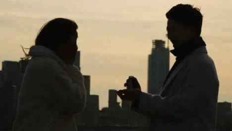 Silhouette Of Couple With Romantic Man Proposing To Woman Against City Skyline