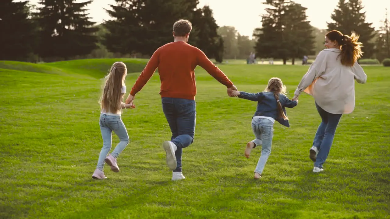 Back View Of Happy Family Holding Hands And Running Together In The Park