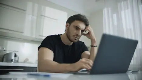 Young man typing laptop computer at home Pensive businessman using computer