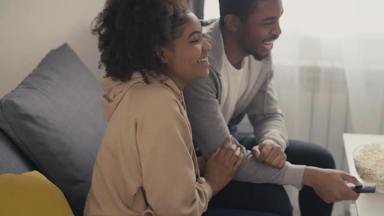 Young Couple Laughing While Watching A Programme On Tv