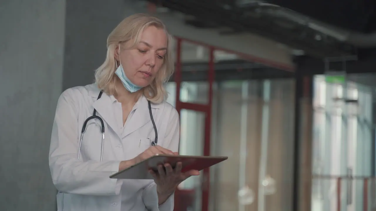 A Blonde Middle Aged Female Doctor Consults Data On A Tablet