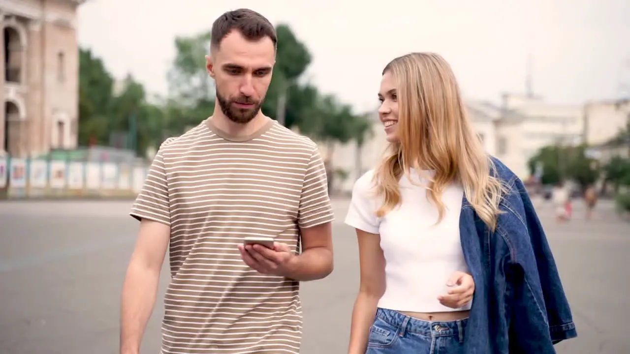 Two Young Friends Looking At The Phone And Walking Down The Street