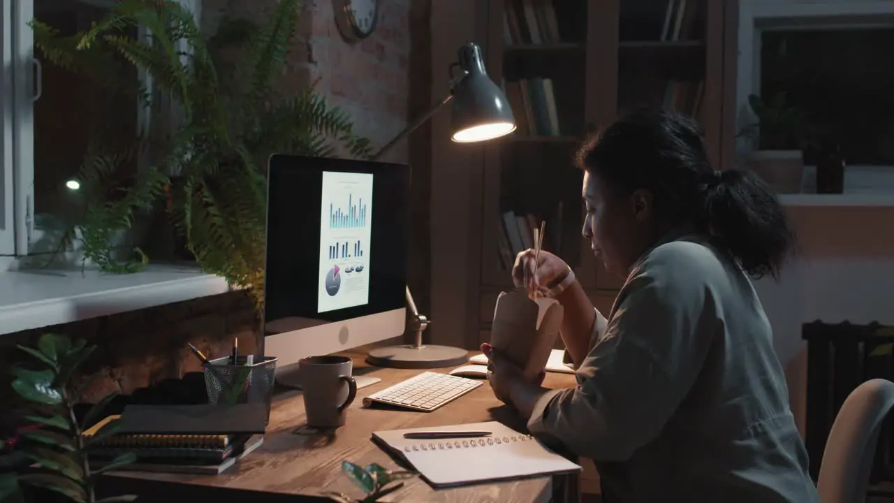 Brunette Woman Sitting In Front Of Computer While Eating Food And Working