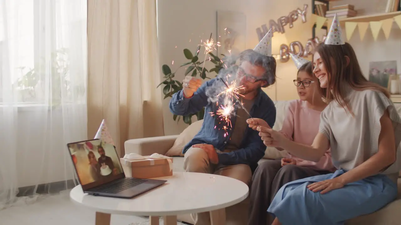 Parents And Daughter Celebrating Birthday Online Wearing Birthday Hats And Waving Sparkles