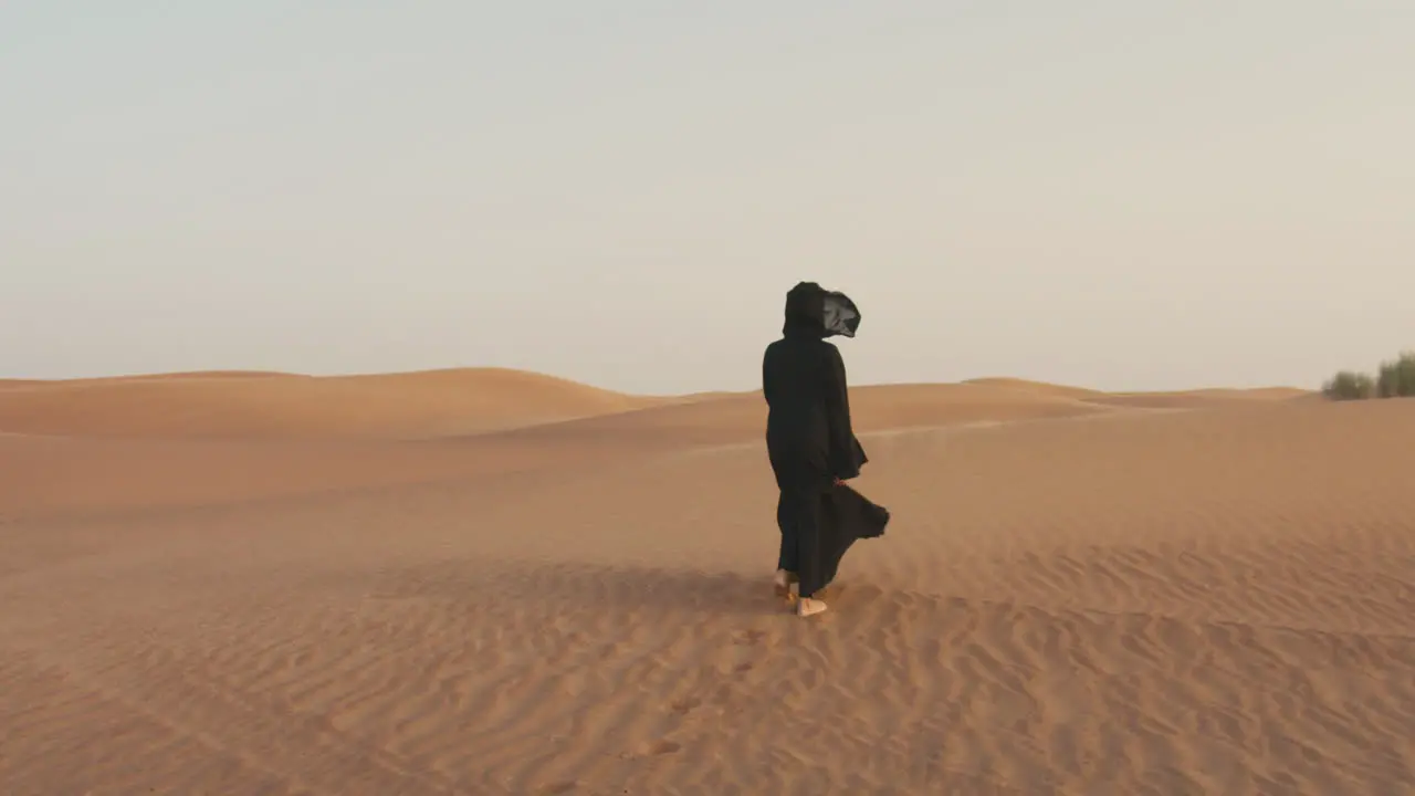 Back View Of A Muslim Woman With Hijab Walking Barefoot In A Windy Desert