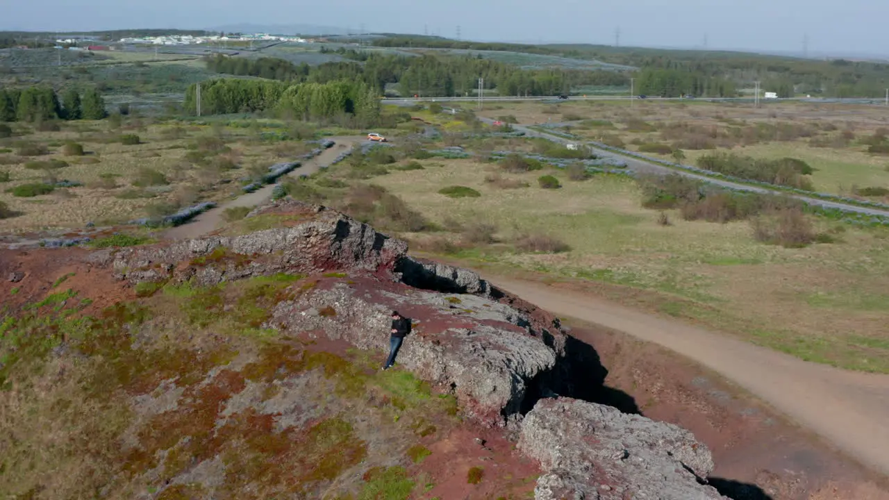 Aerial view birds eye young man explorer relaxing after climbing red rock formation in Iceland Drone view male hiker using smartphone taking a break enjoying beauty in nature