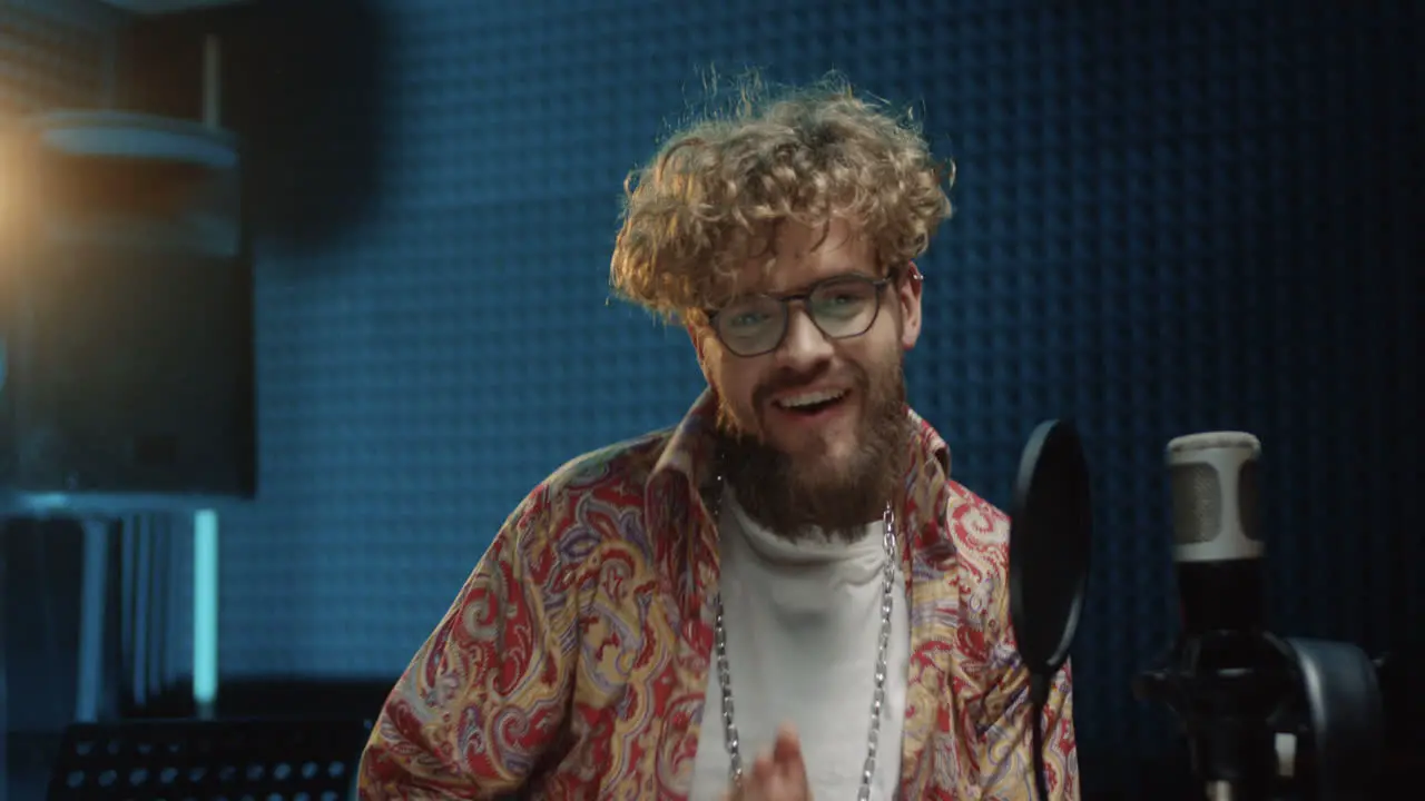 Young Stylish Hipster Male Singer In Glasses And With Curly Hair Psing To The Camera Cheerfully And Blowing Kisses While Standing At The Mic In The Sound Studio