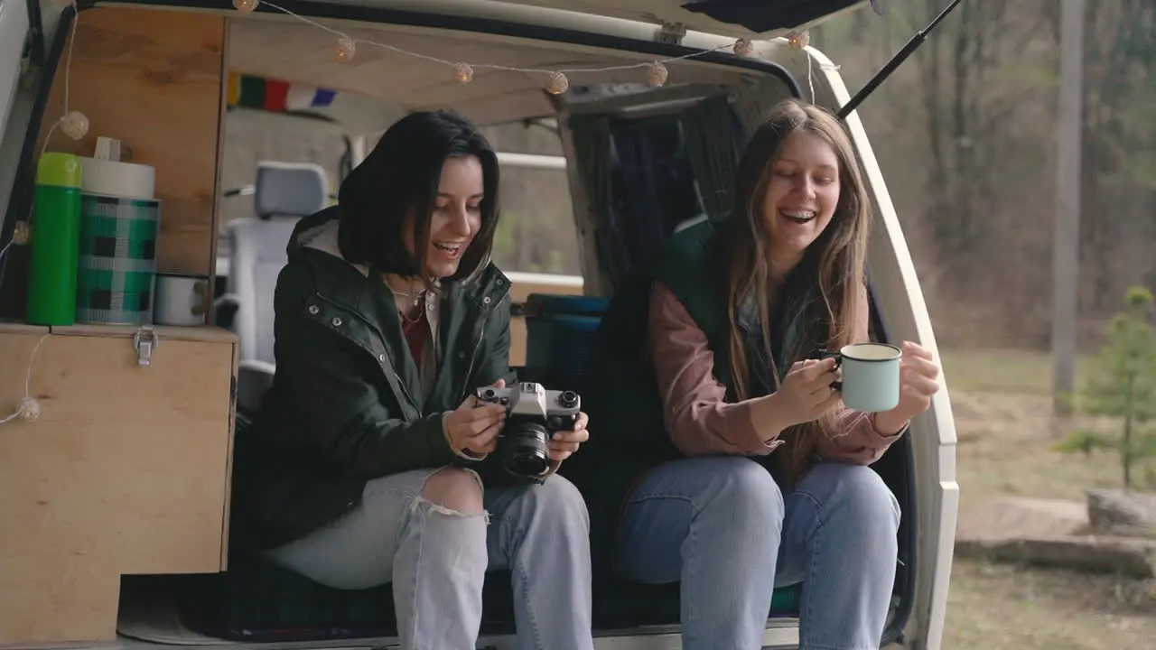 Two Young Girl Friends Chat In The Back Of A Caravan In The Middle Of The Forest