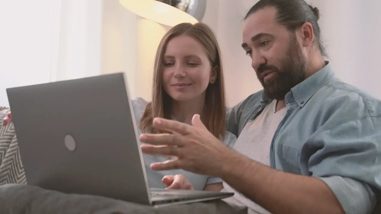 A Happy Couple Have A Relaxed Conversation Sitting On The Sofa And Looking At The Laptop 1