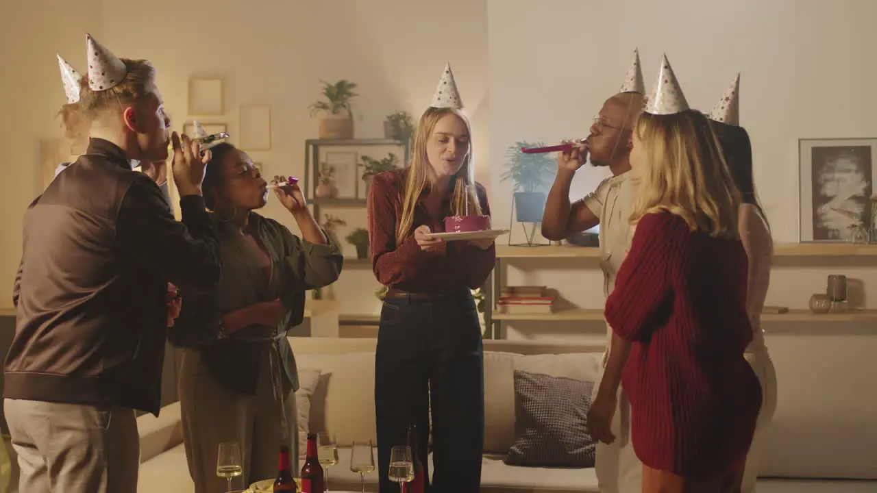 Group Of Friends In Birthday Party Girl Blows Out A Candle On The Birthday Cake Making A Wish 1