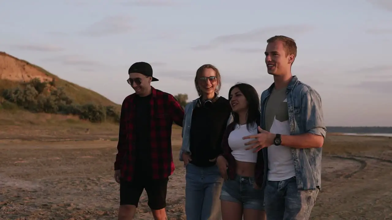 Group Of Young People Walking By Sandy Road Near The Sea Or Lake