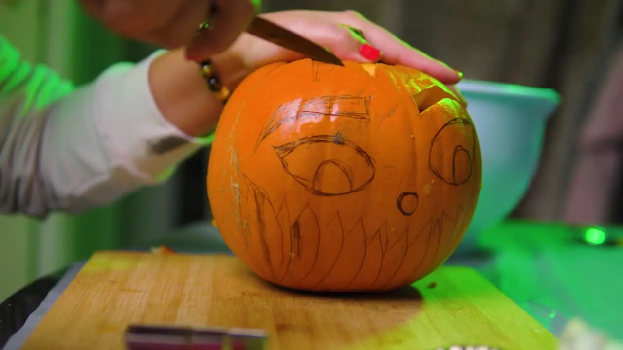 Woman with red nails carving eyebrow into the pumpkin with colourful background