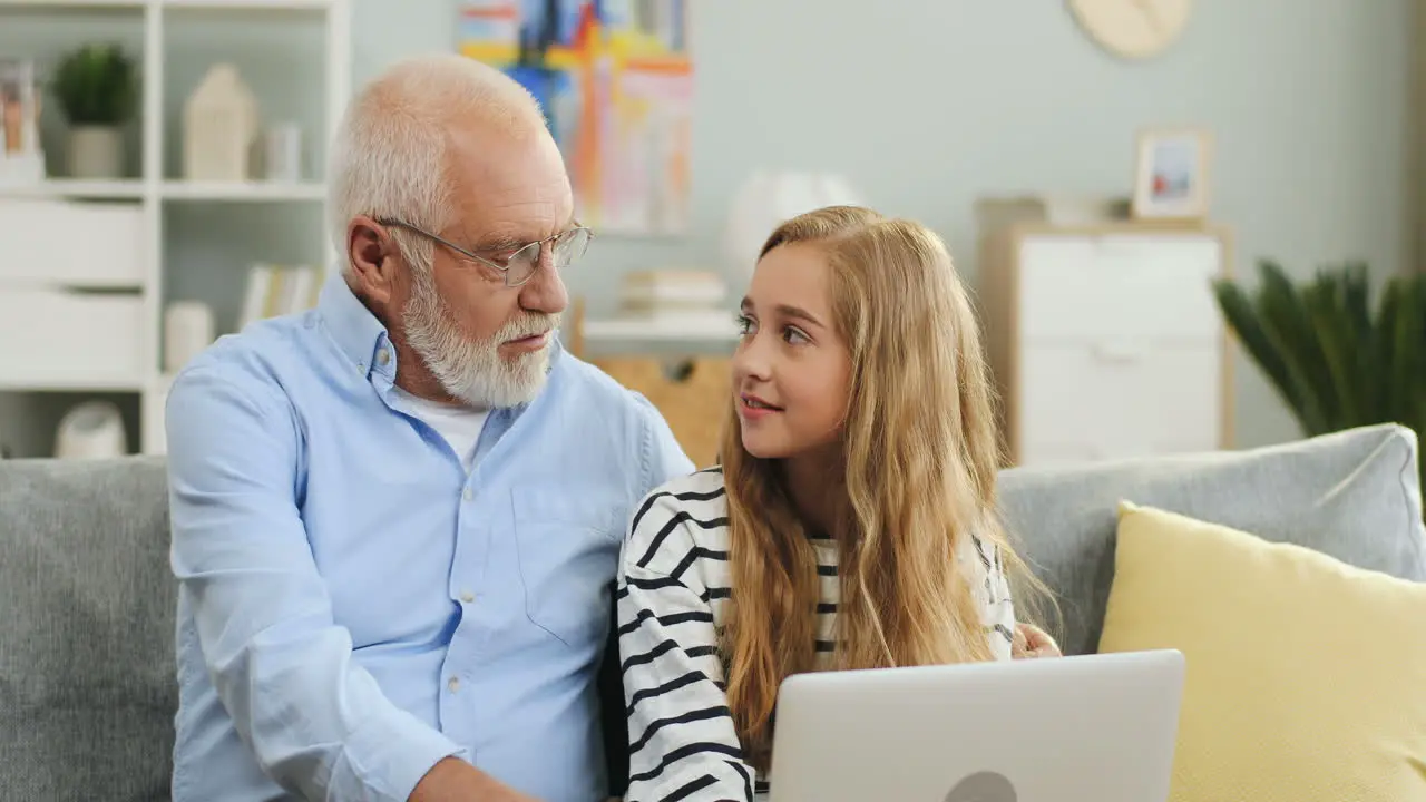 Close Up Of The Grey Haired Man In Glasses Looking On The Laptop Screen On Which His Granddaughter Playing Or Watching Something