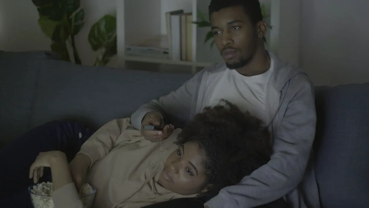 Young Couple Picking A Movie With The Remote Control And Eating Popcorn In The Dark