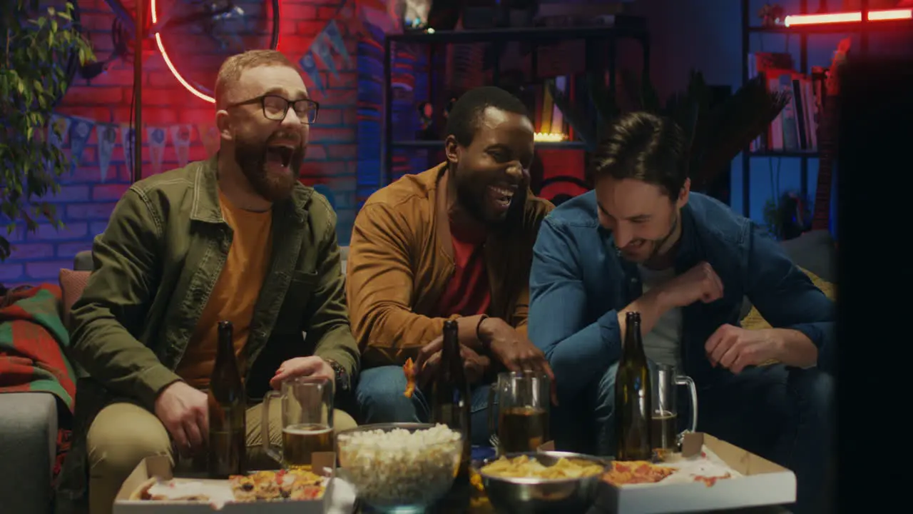 Portrait Shot Of The Mixed Races Young Men Watching Tv Together And Laughing While Making Jokes On The Sofa At Home At Night