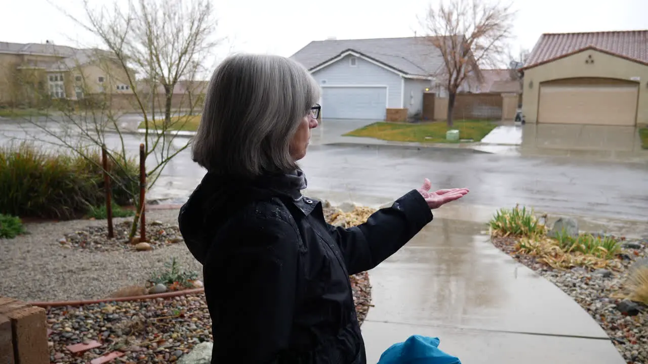 A middle aged woman checking the weather and feeling the winter rain drops with her hand in slow motion