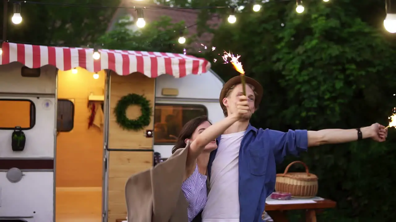 Young Couple Embracing Standing In Front Trailer They Living In With Sparklers Celebrating Waving Hands With Fireworks Sticks