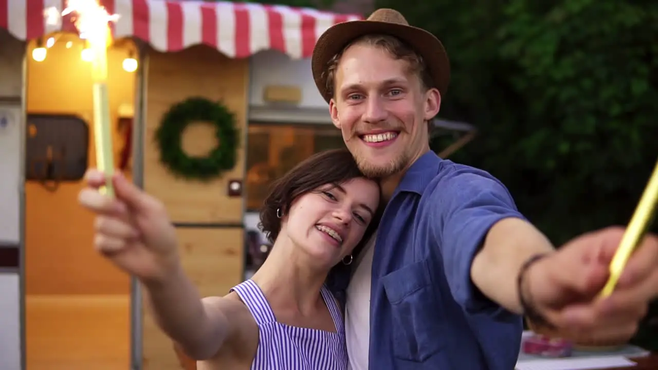 Portrait Of A Good Looking Couple Embracing Standing With Sparklers Celebrating Waving Hands With Fireworks Sticks