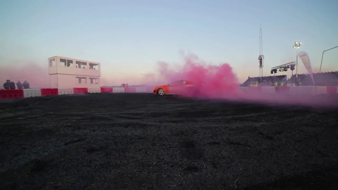 Orange Nissan Skyline R34 doing a massive burnout with pink smoke from the tyres