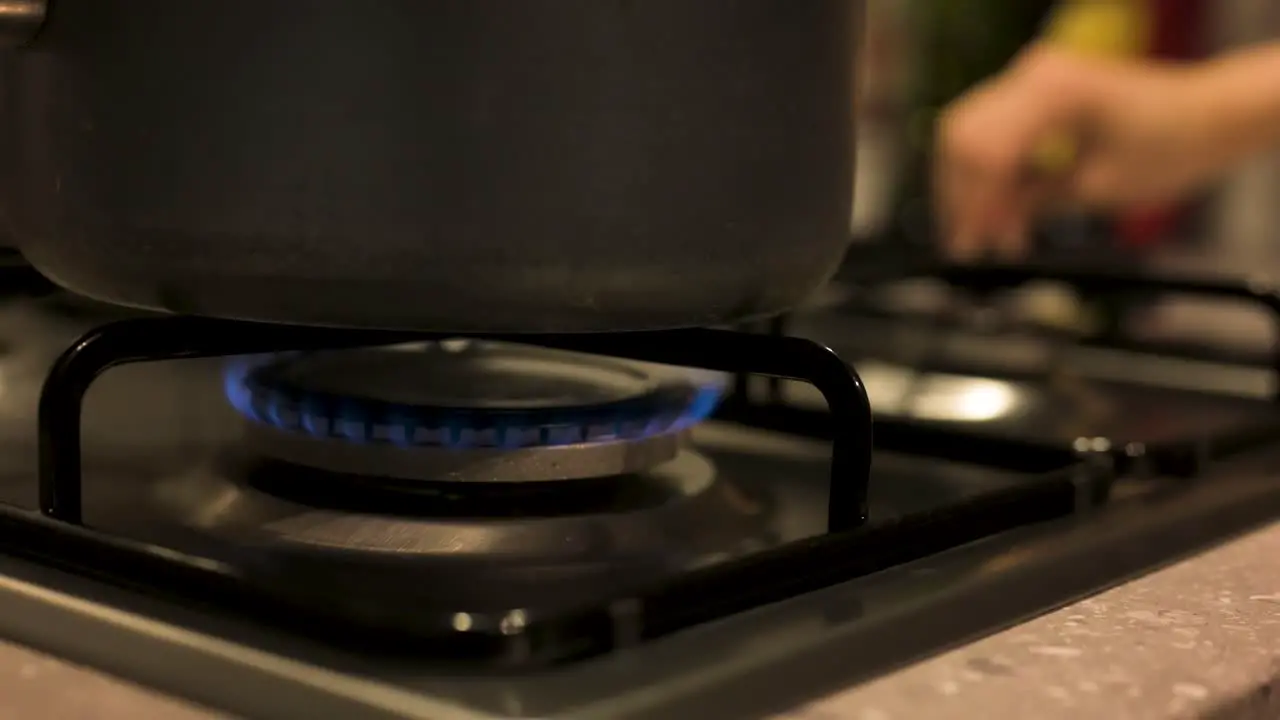 Turning gas stove down with pot on top close up slow motion