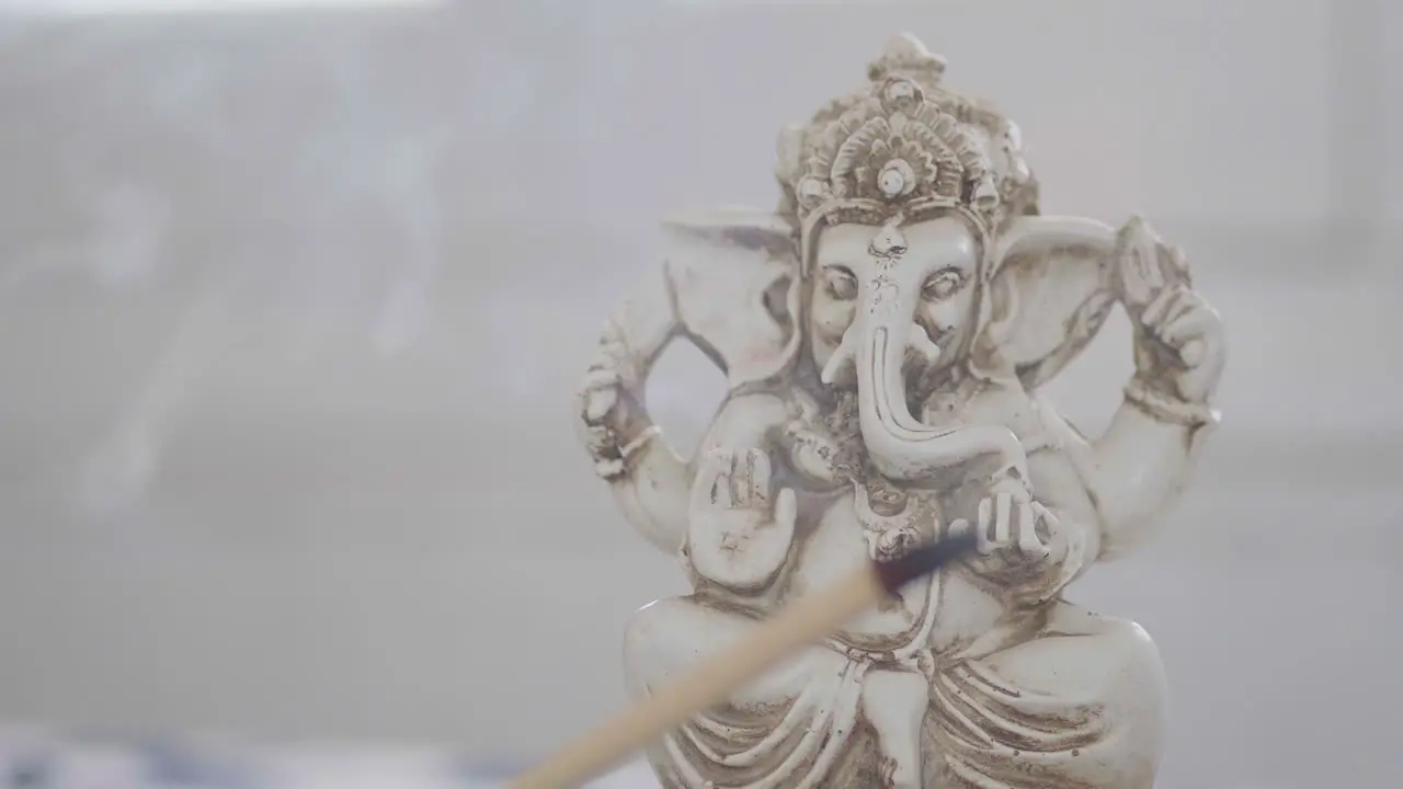 Close-up of a Ganesha figurine behind a burning incense