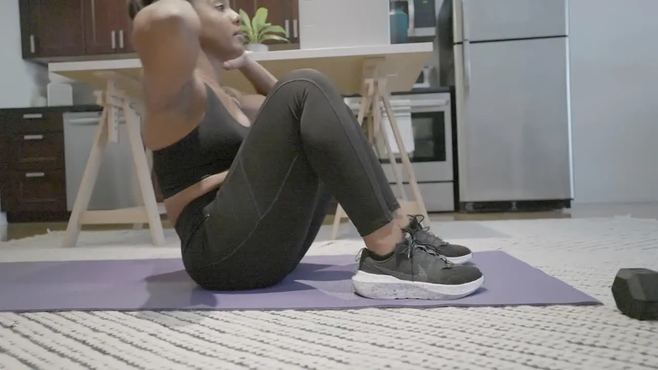 A sliding shot of a black female doing sit ups in her kitchen