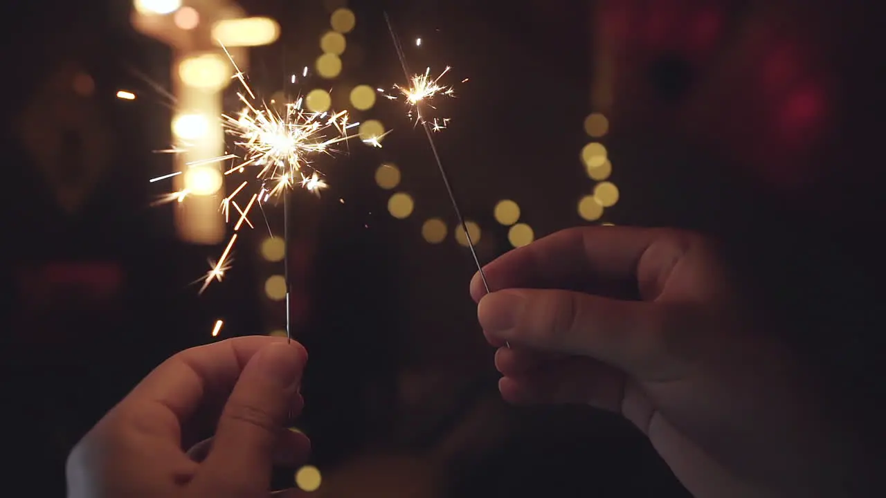 Hands holding bright sparklers burning down in slow motion