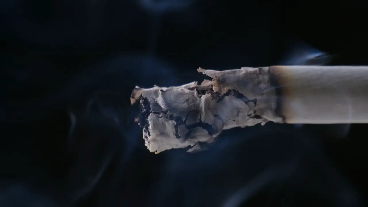 A Cigarette smoking closeup paper burning with black background Ashes and Smoke are visible with soft Light on the Cigarette