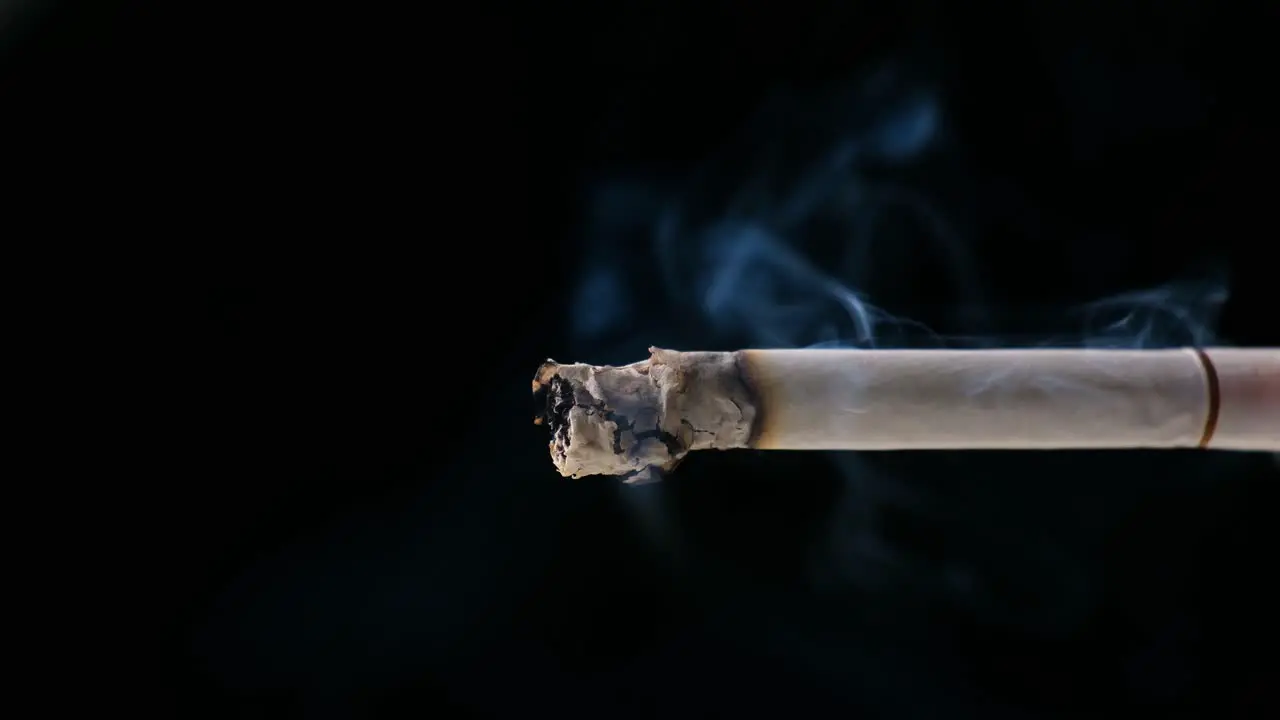 A Cigarette smoking with black background Ashes and Smoke are visible with soft Light on the Cigarette