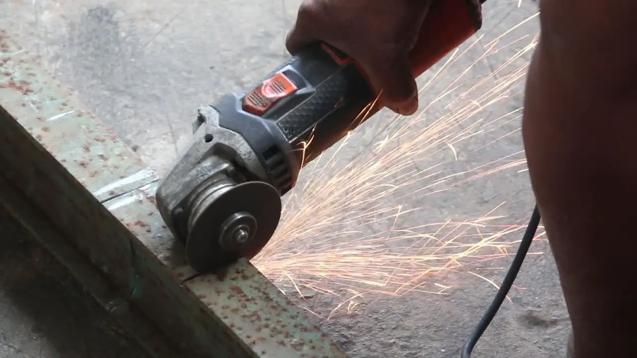 close up shot of a hand using an angle grinder to cut a metal bar producing lot of sparks with no protection or gloves in his hand